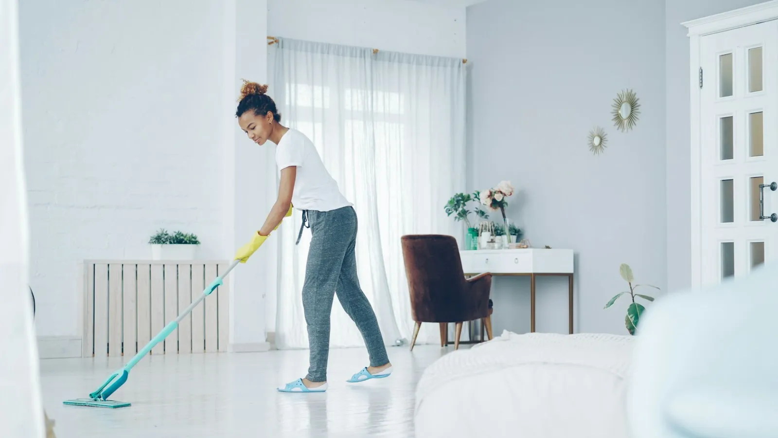 A cleaner in yellow gloves mopping the floor of a bright living room